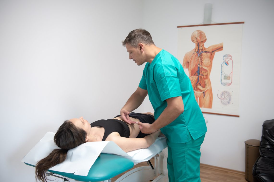 kinetoterapeut aplicand drenaj limaftic manual pe abdomenul unei paciente intinse pe masade tratament
