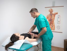 kinetoterapeut aplicand drenaj limaftic manual pe abdomenul unei paciente intinse pe masade tratament