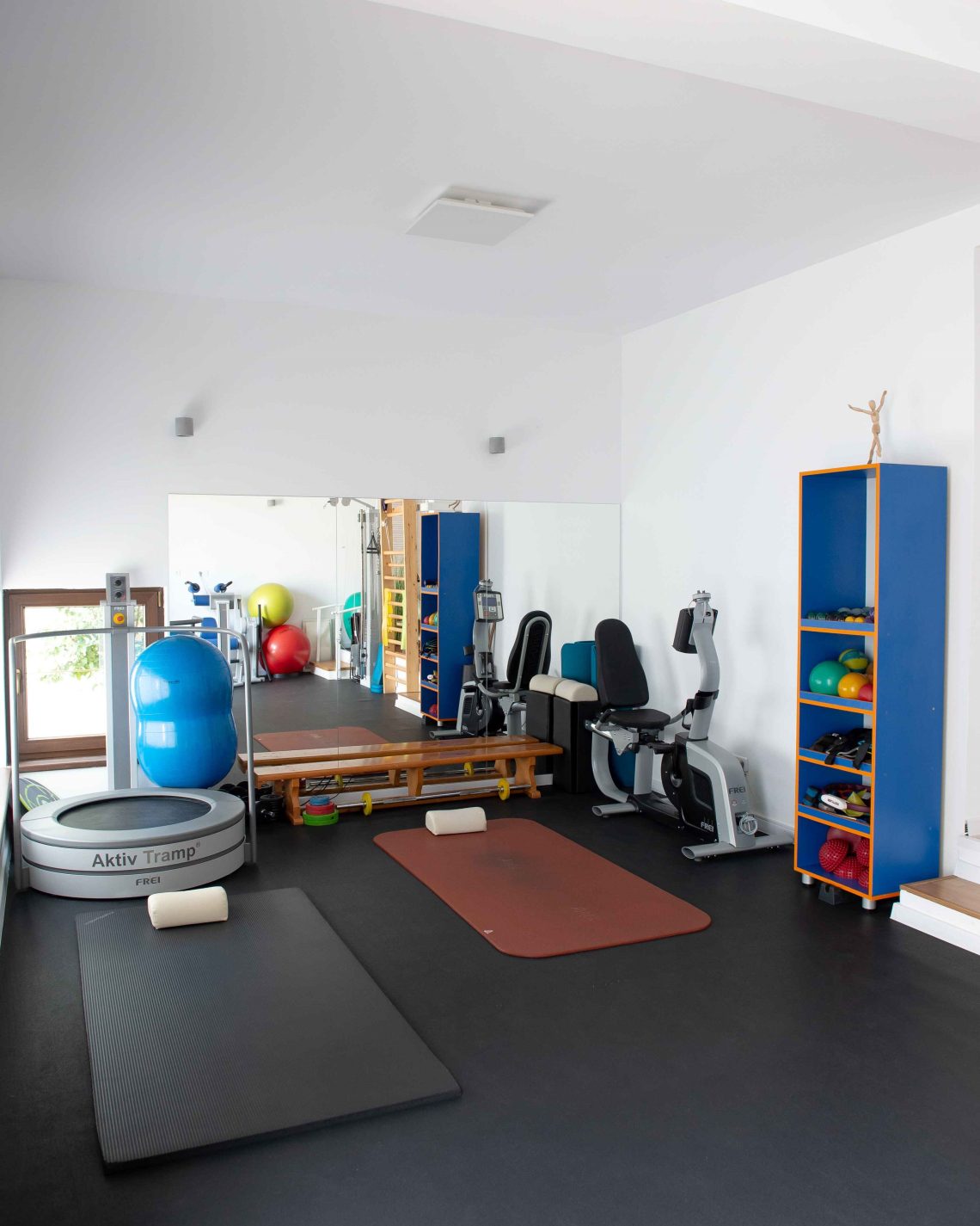 Vedere de ansamblu asupra salii de recuperare medicala, cu bicicleta, saltele, mingi de gimnastica, trambulina si rafturi cu echipamente de kinetoterapie