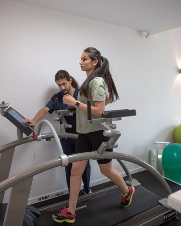 kinetoterapeut monitorizand o pacienta in timpul unui exercitiu de reeducarea mersului pe banda de alergare intr-o sala de recuperare medicala