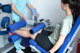 Kinetoterapeut supravegheaza o pacienta in timpul unui exercitiu la aparat pentru intarirea musculaturii membrelor inferioare