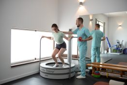 pacienta supravegheata de kinetoterapeut in timpul unui exercitiu de stabilizare a genunchilor pe trambulina Akitv Tramp intr-o sala de recuperare