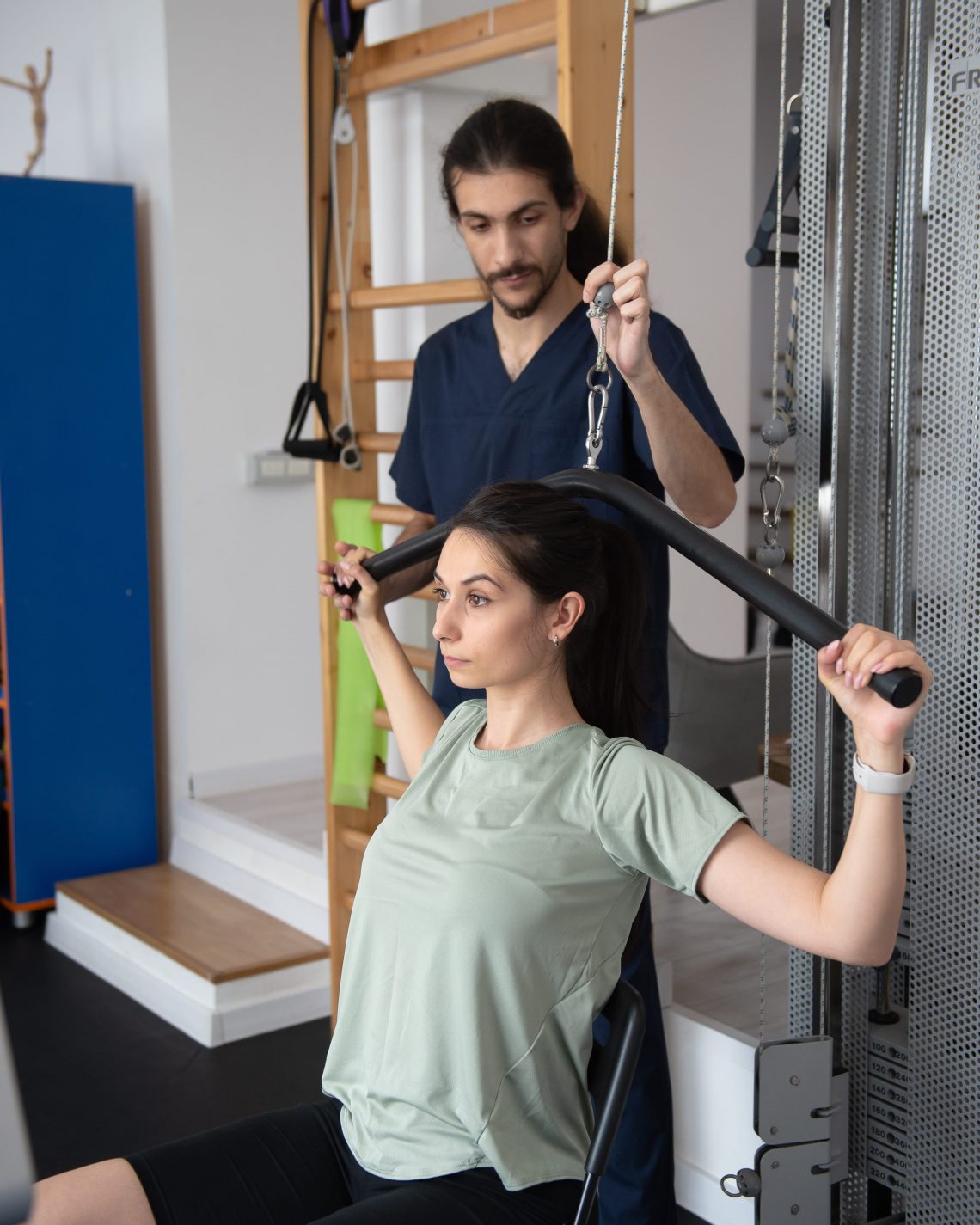 Pacienta executa un exercitiu de tractiune la aparat sub supravegherea kinetoterapeutului