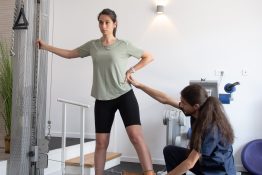 Terapeutul asista pacienta in realizarea unui exercitiu de tonifiere a membrului inferior folosind un aparat cu cablu