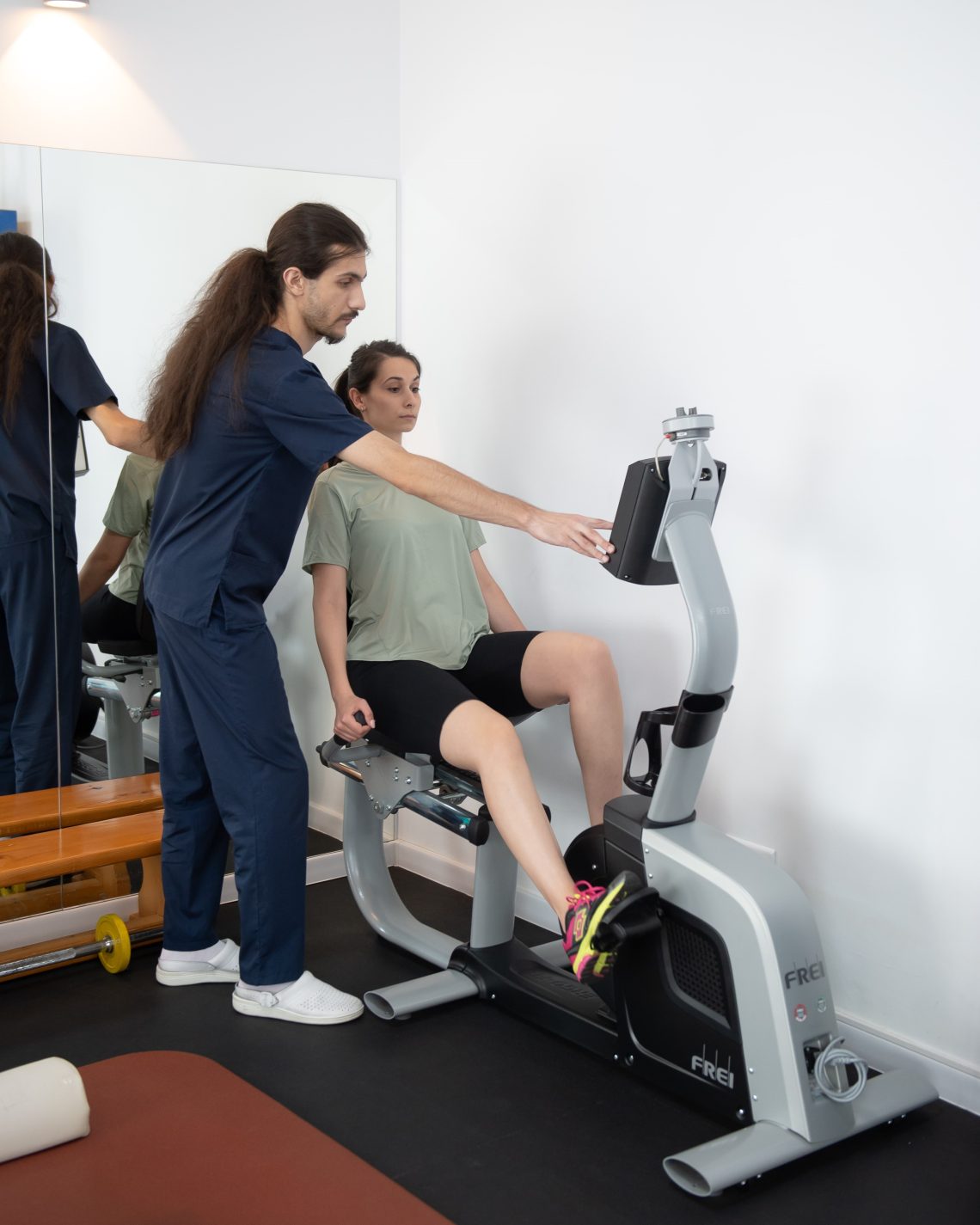 kinetoterapeut asistand pacienta in timpul unui exercitiu controlat pe bicicleta medicala pentru tonifiere si recuperare medicala a membrelor inferioare