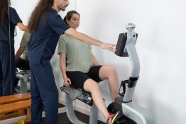 kinetoterapeut asistand pacienta in timpul unui exercitiu controlat pe bicicleta medicala pentru tonifiere si recuperare medicala a membrelor inferioare